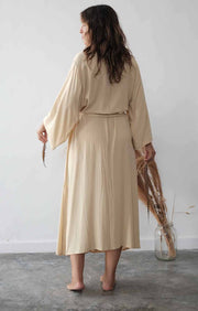 Woman wearing a beige dress holding an umbrella against a white wall.