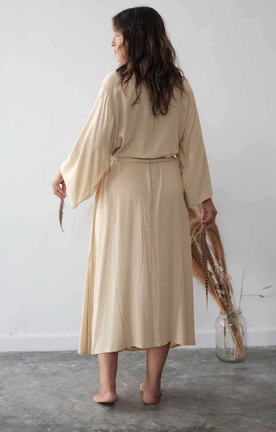 Woman wearing a beige dress holding an umbrella against a white wall.