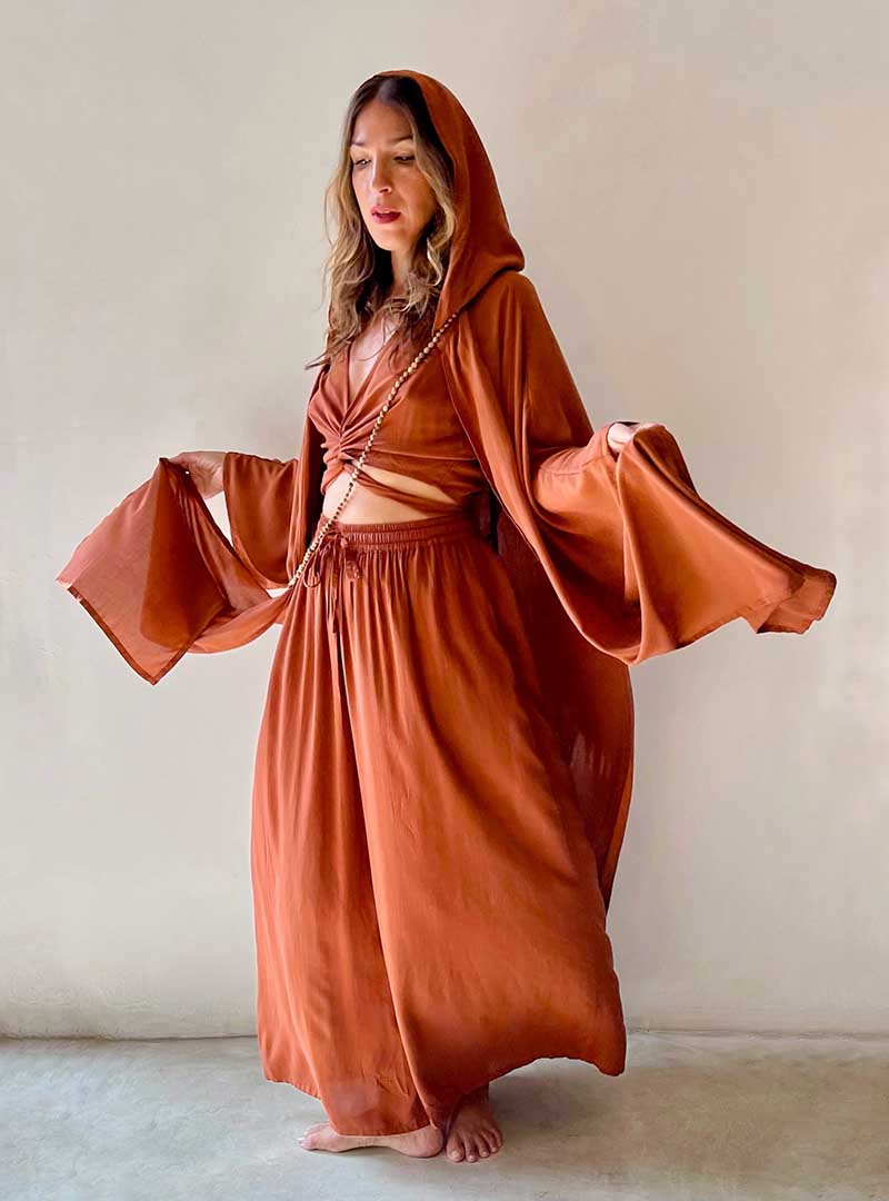 Woman wearing a long, flowing rust-colored dress against a plain background