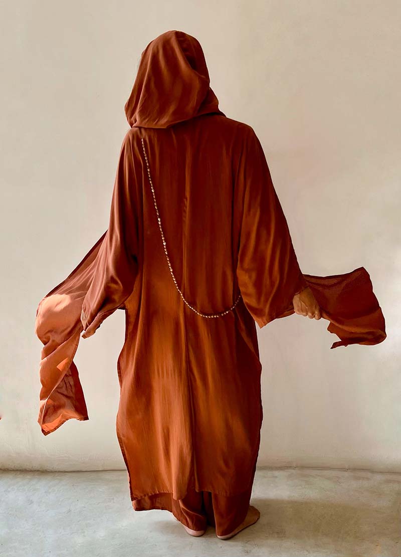 Person wearing a brown hooded garment against a plain background