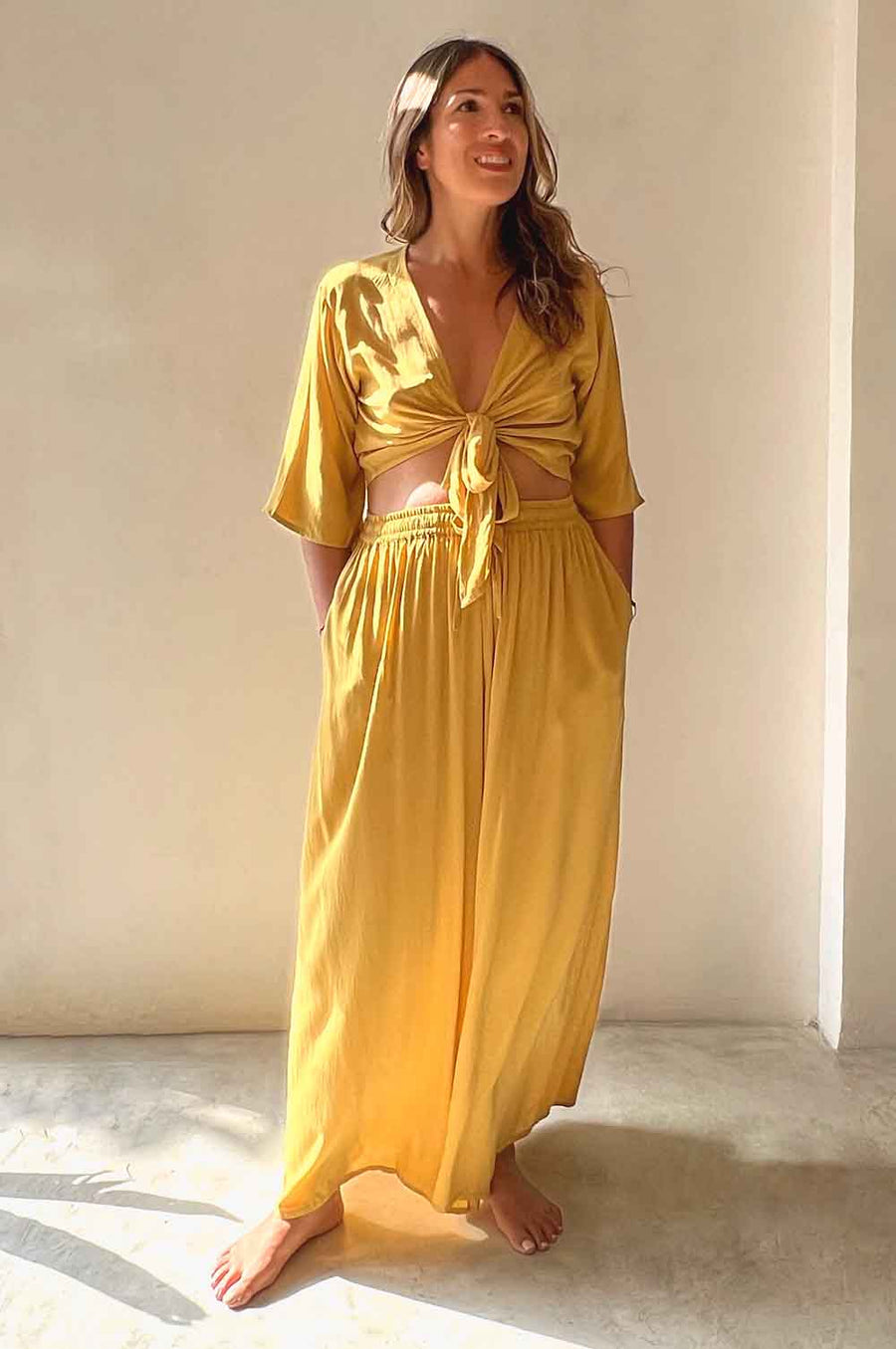 Woman wearing a yellow outfit with a tied top and long skirt against a neutral background