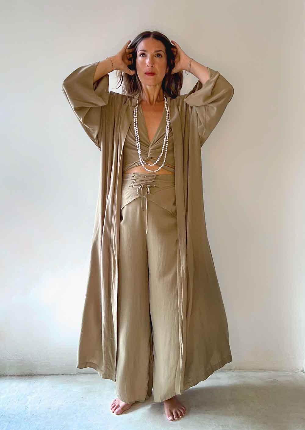Woman wearing a beige outfit with a long duster and wide-leg pants against a plain background
