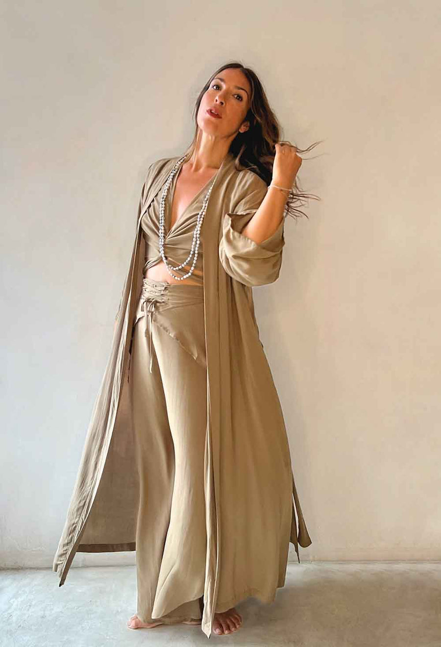 Woman wearing a beige outfit with a long duster against a plain background