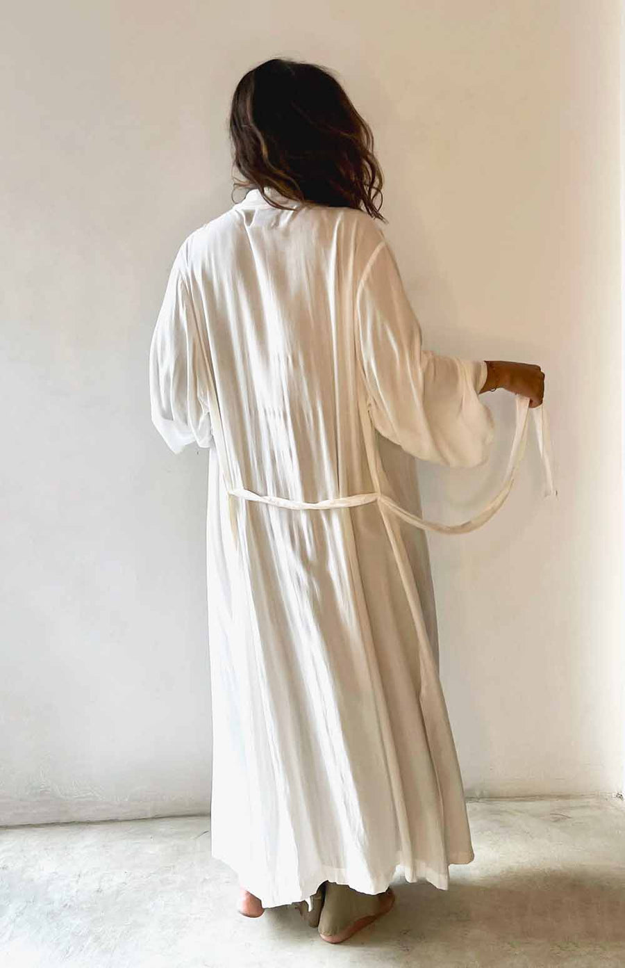 Person wearing a long white robe against a plain background