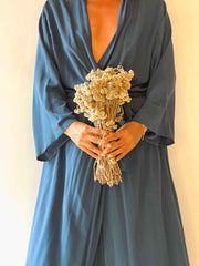 Person wearing a long, dark blue dress holding a bouquet of dried flowers against a beige background