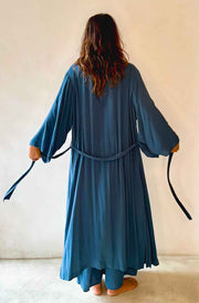Person wearing a long blue dress with a belt, standing against a plain background