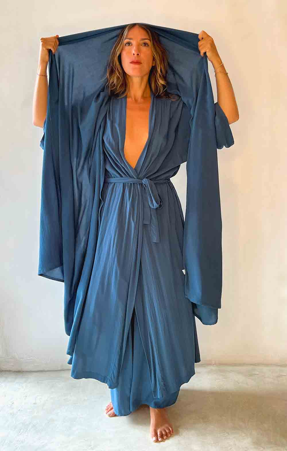 Woman holding a blue robe over her head against a plain background