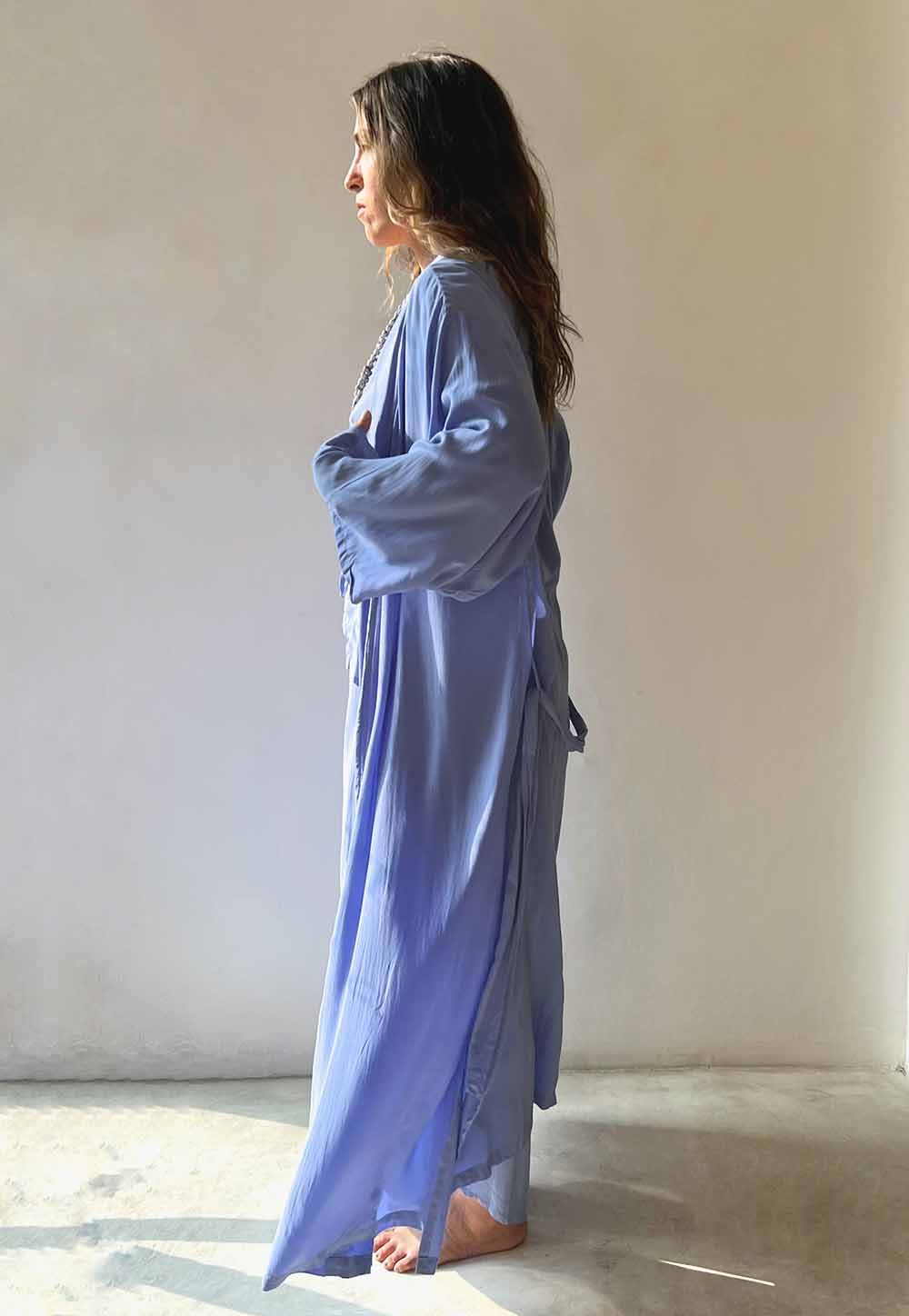 Woman wearing a long blue dress standing against a plain white wall.