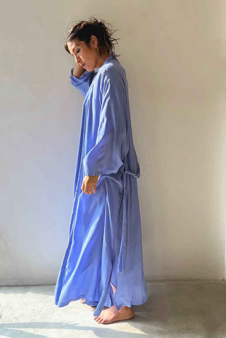 Woman wearing a long blue robe against a plain wall.