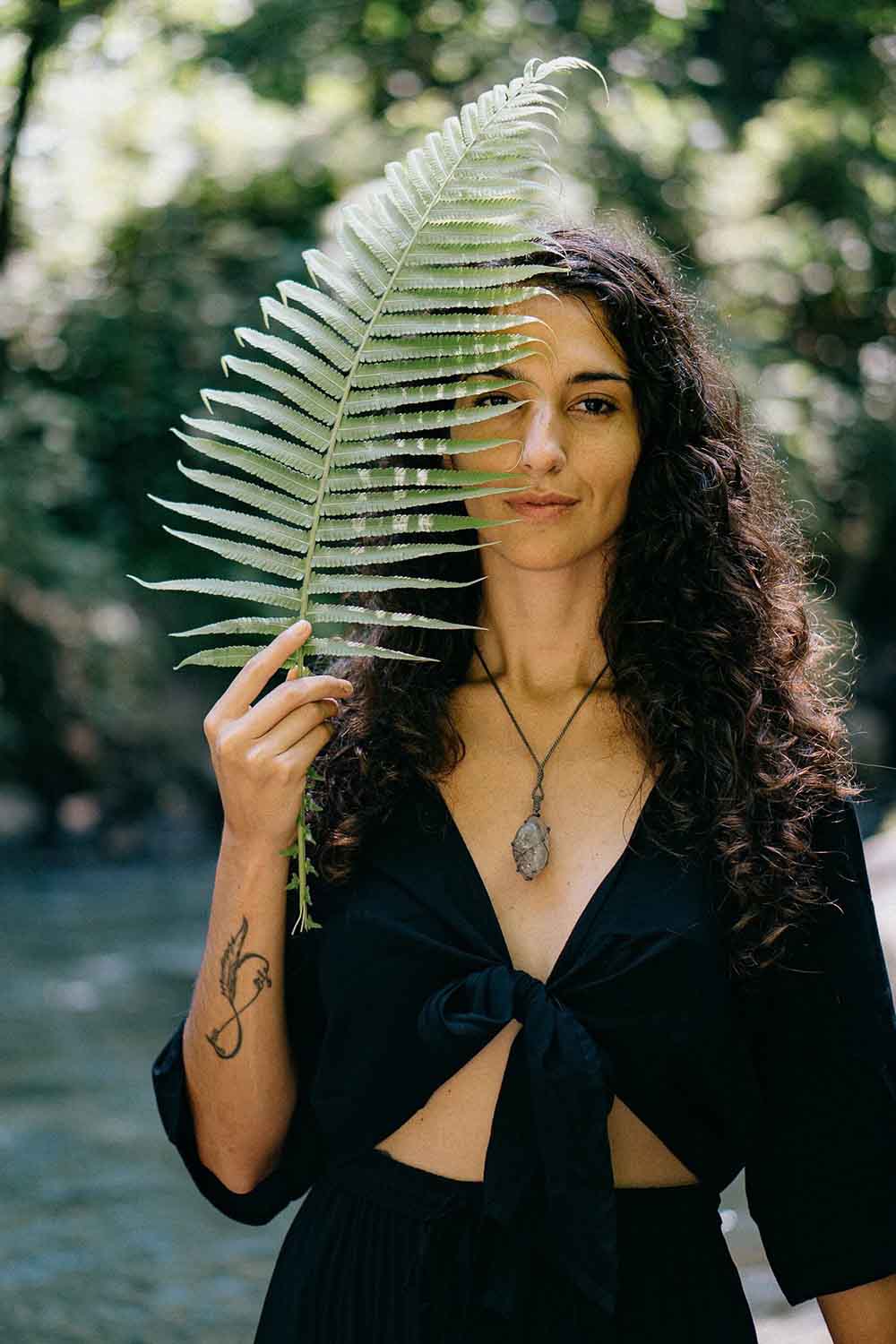 Woman holding a fern leaf in front of her face with a blurred natural background