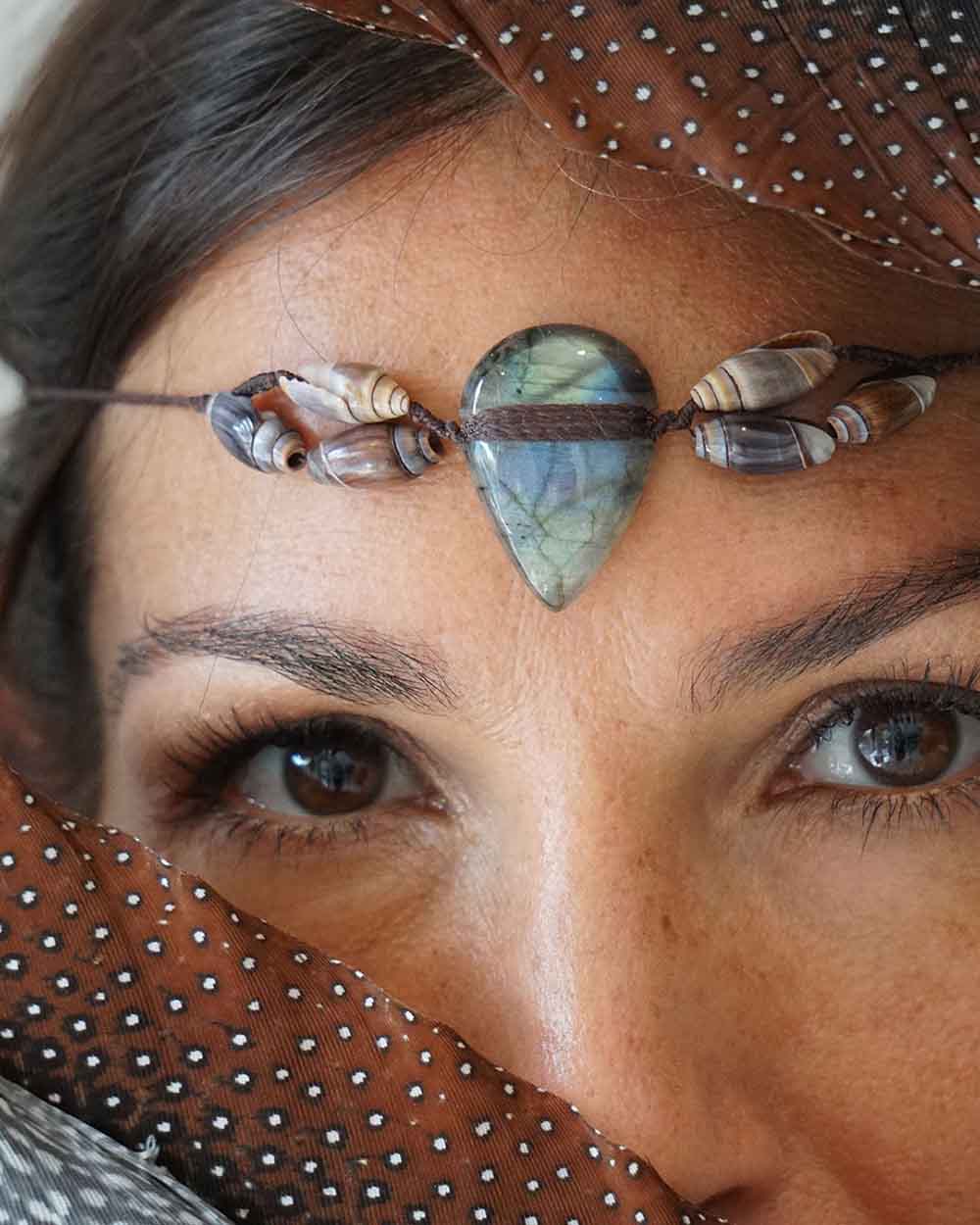 Close-up of a person wearing a decorative headband with a heart-shaped stone and feathers.