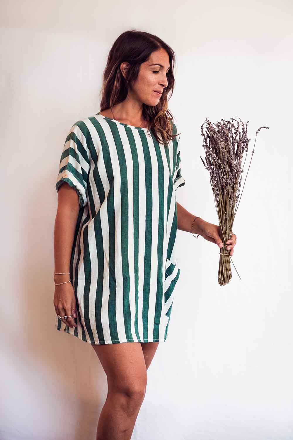 Woman wearing a green and white striped dress holding dried lavender on a plain background