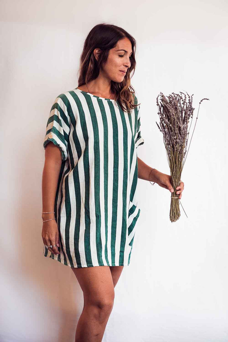 Woman wearing a green and white striped dress holding dried lavender on a plain background