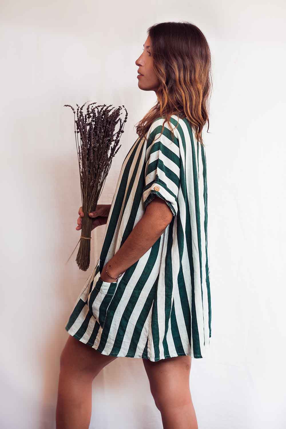 Woman wearing a green and white striped dress holding dried plants against a plain background