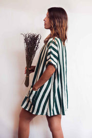 Woman wearing a green and white striped dress holding dried plants against a plain background