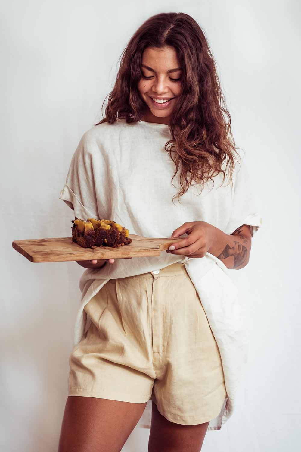 Woman holding a wooden tray with food against a plain background