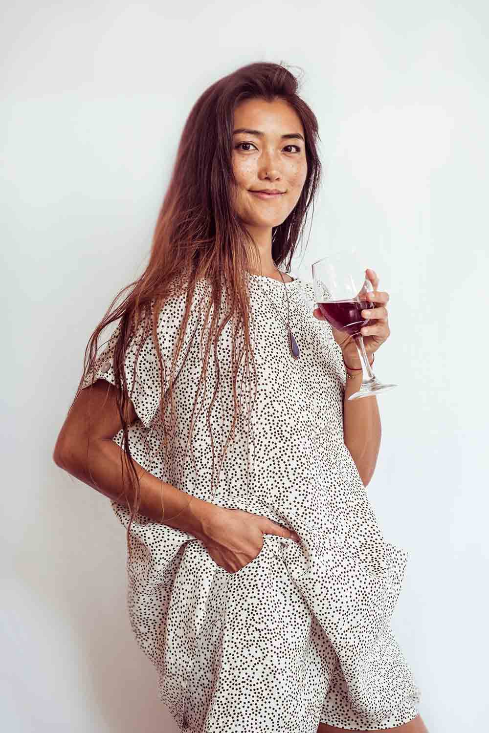 Woman in a patterned dress holding a glass of red wine against a white background
