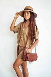 Woman wearing a beige outfit with a straw hat and brown leather bag on a white background