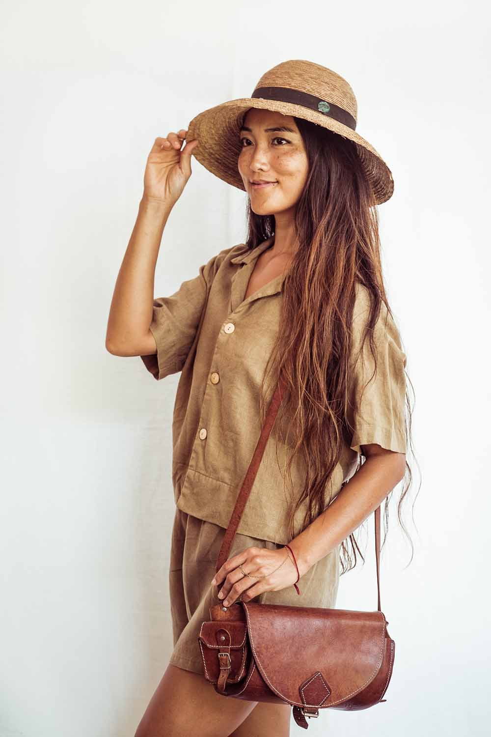 Woman wearing a brown hat and outfit, holding a brown leather bag against a white background