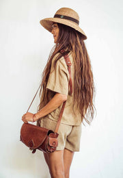 Woman wearing a straw hat and carrying a brown leather bag against a white background