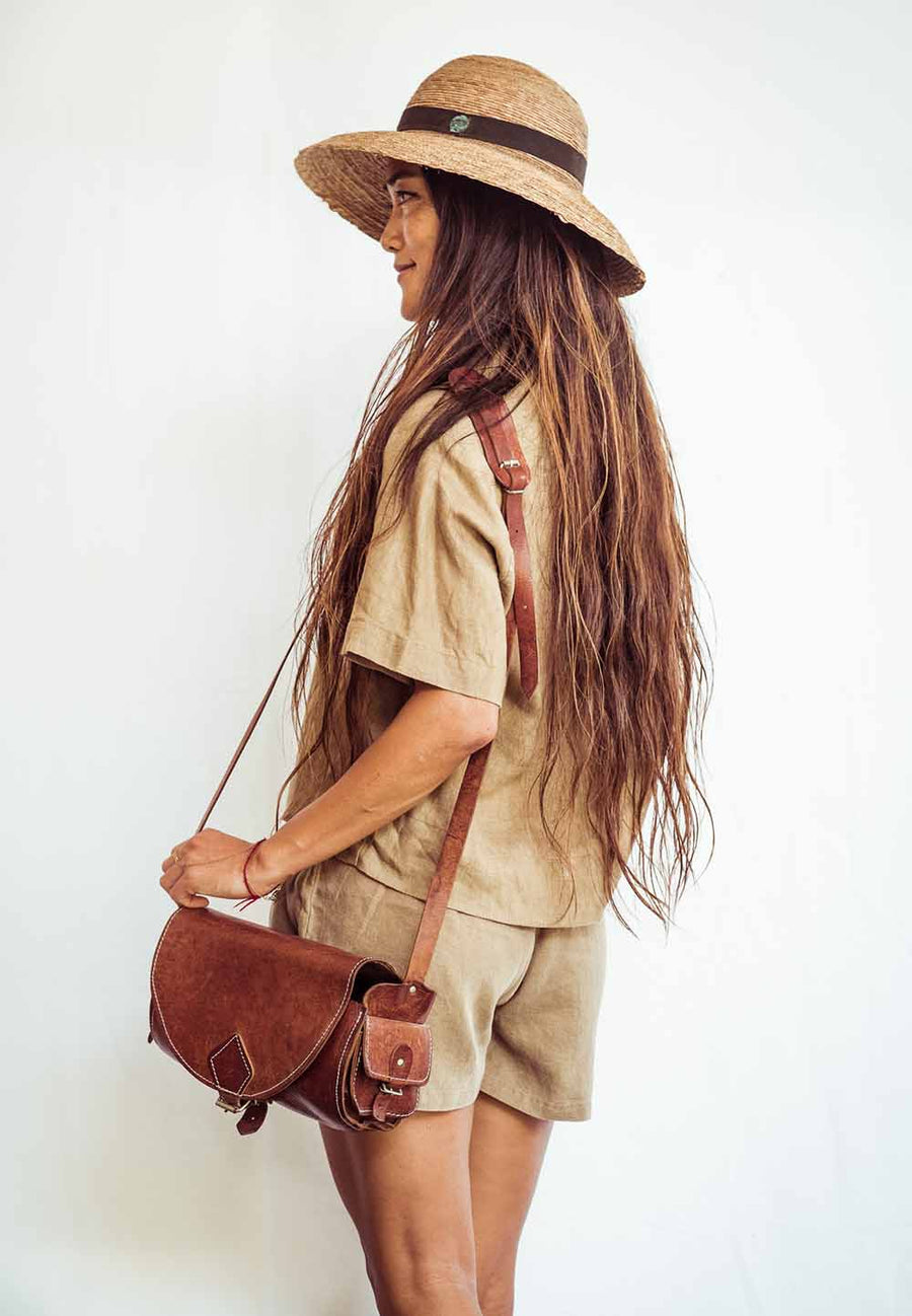 Woman wearing a straw hat and carrying a brown leather bag against a white background