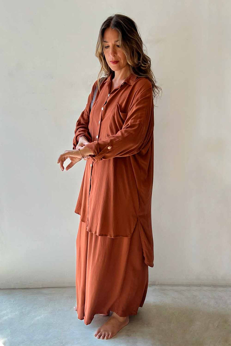 Woman wearing a long rust-colored dress against a plain background