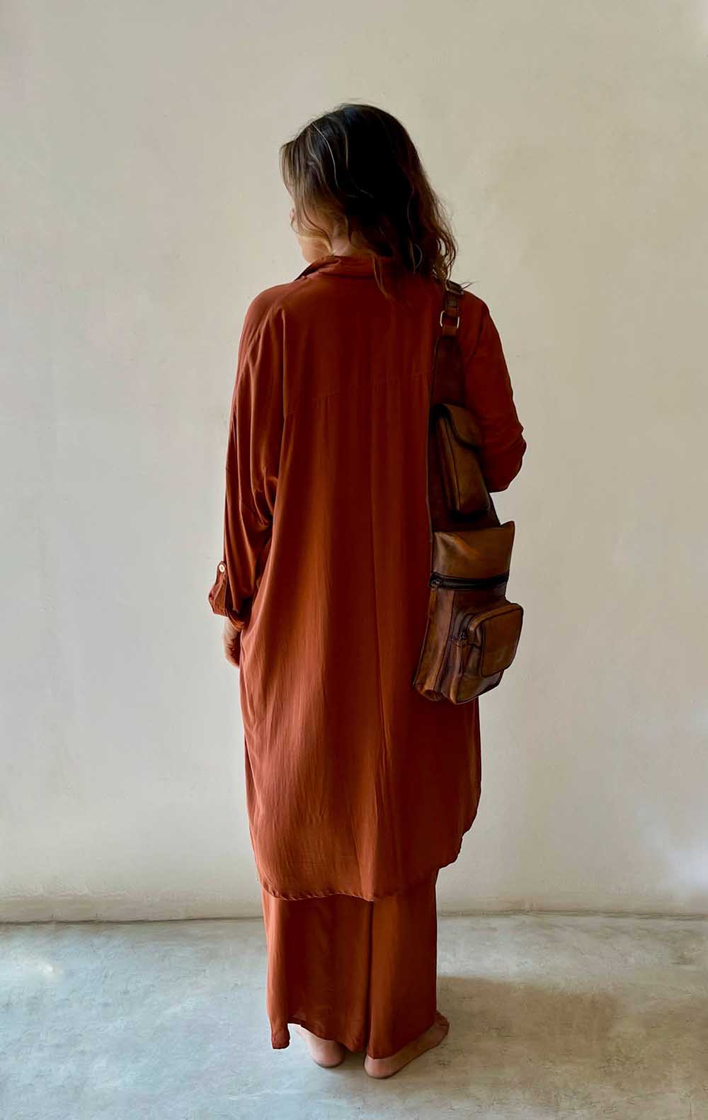 Person wearing a rust-colored outfit with a brown bag against a plain background