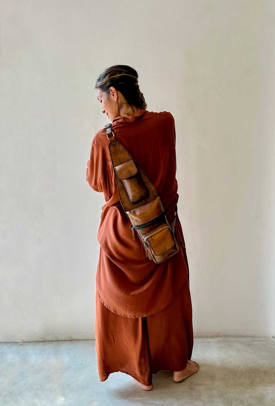 Person wearing a rust-colored dress with a brown leather bag against a plain wall.