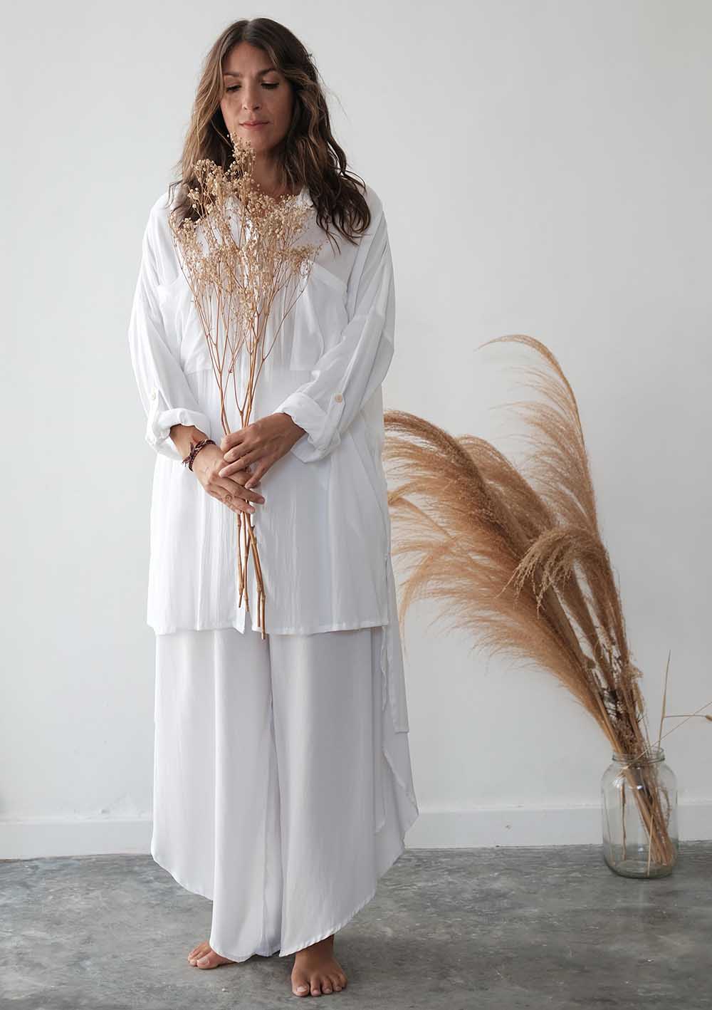 Woman in a white outfit holding dried plants against a plain background