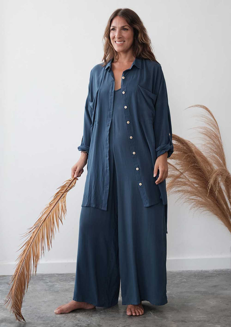 Woman wearing a blue pajama set holding dried pampas grass against a white wall.