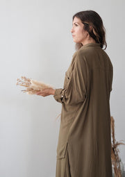 Woman in a long brown dress holding dried flowers against a plain background