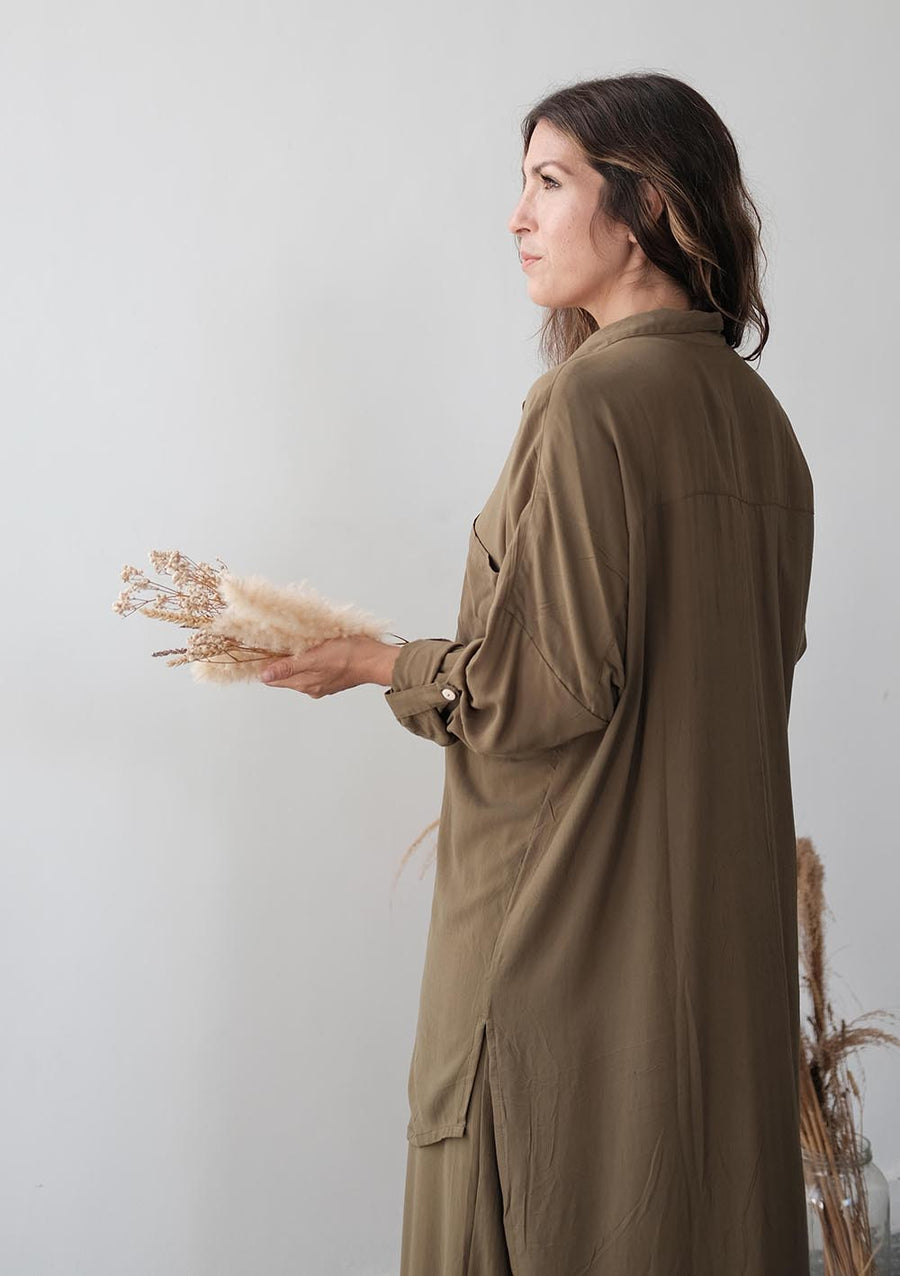 Woman in a long brown dress holding dried flowers against a plain background