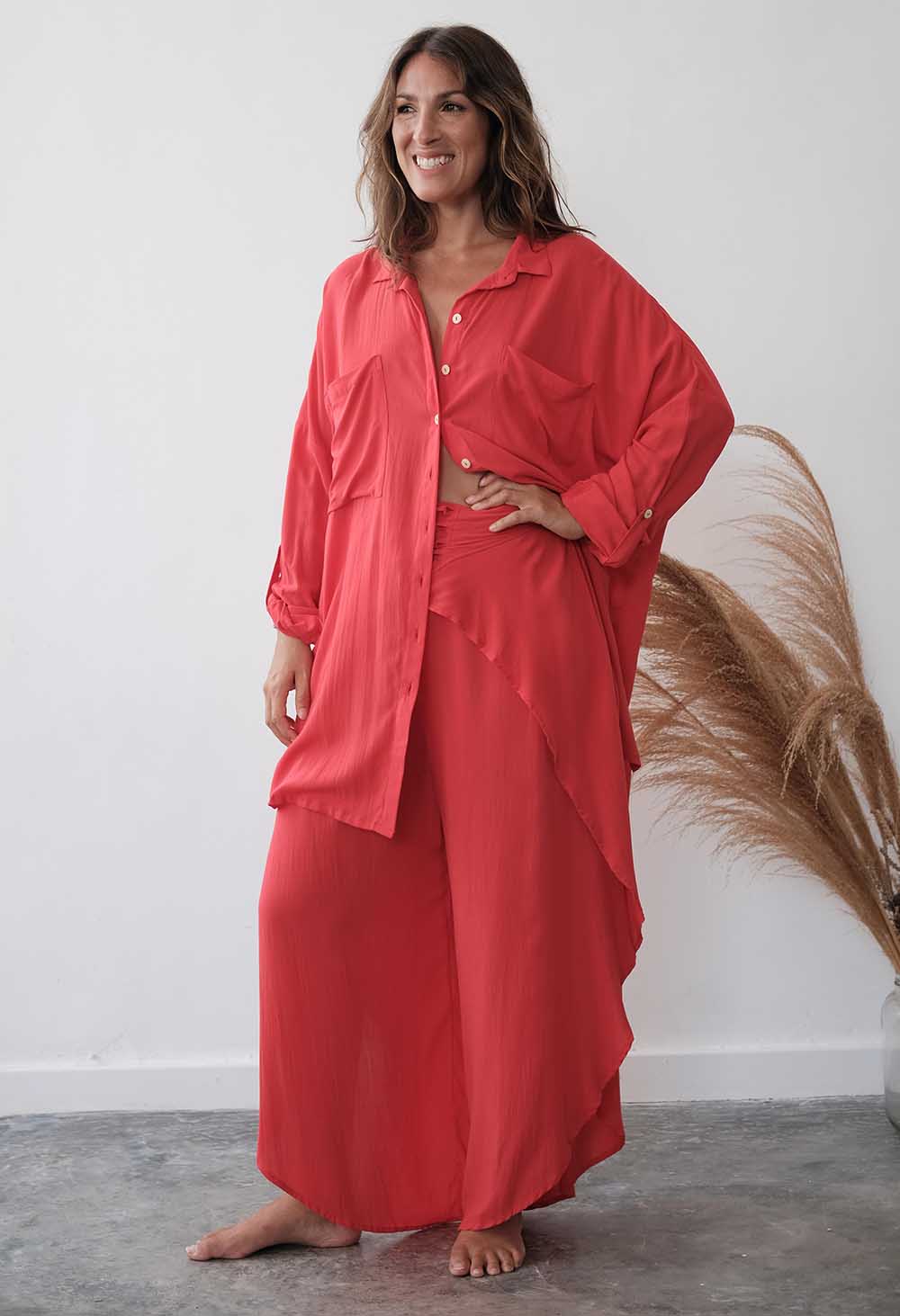 Woman wearing a coral outfit standing against a white wall with decorative elements.