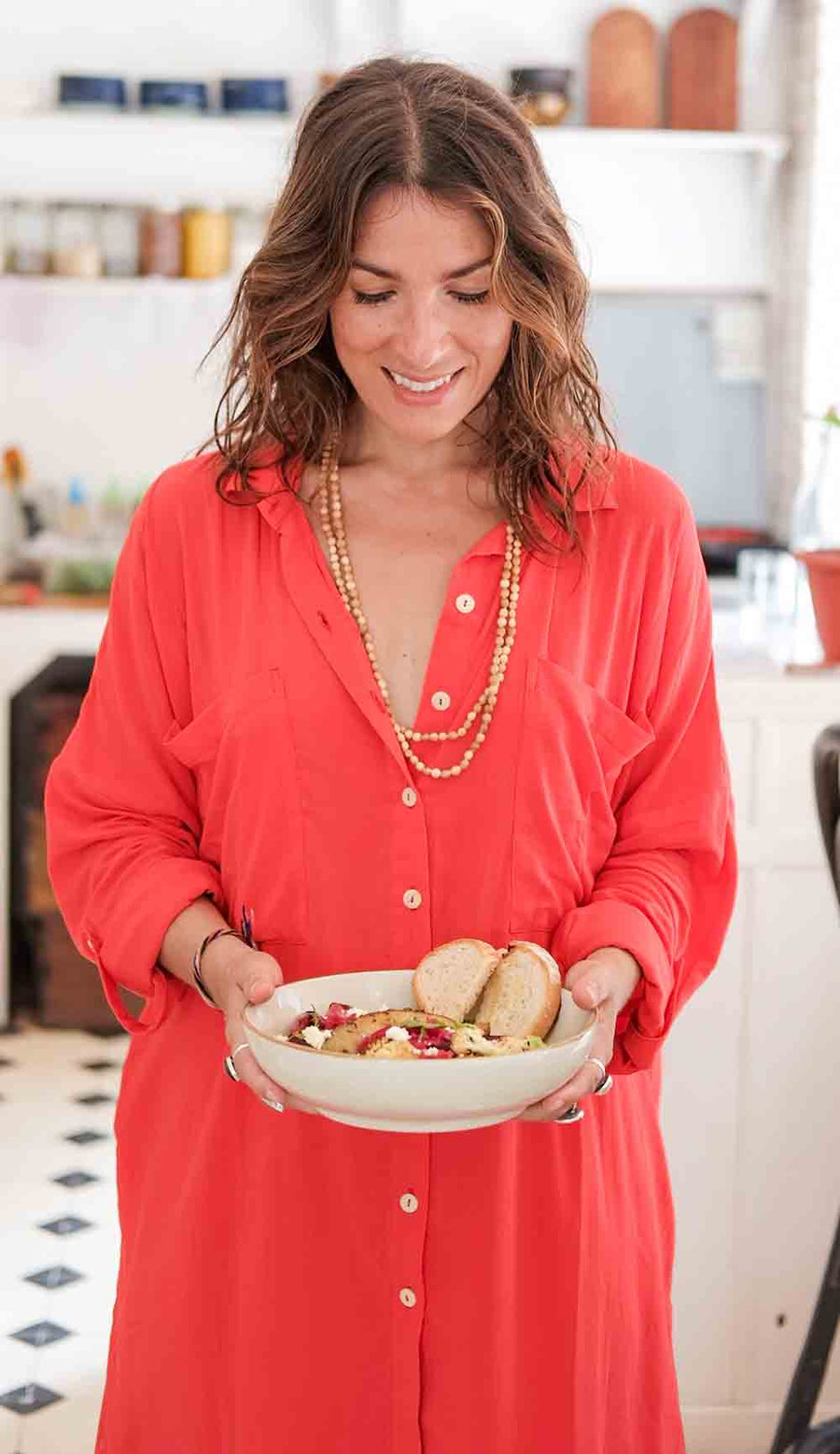 Woman in a red dress holding a bowl of food in a kitchen.