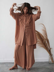 Woman in a brown outfit standing next to pampas grass against a white wall
