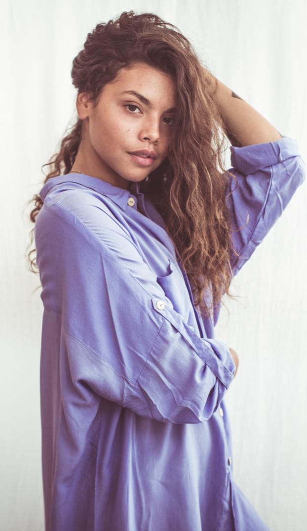 A woman wearing a sky blue, long-sleeved shirt dress with chest pockets and light coconut organic buttons.