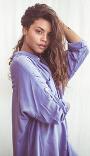 A woman wearing a sky blue, long-sleeved shirt dress with chest pockets and light coconut organic buttons.
