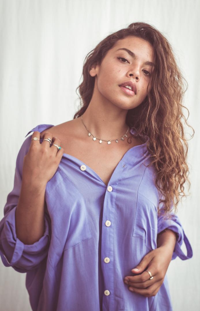 A woman wearing a sky blue, long-sleeved shirt dress with chest pockets and light coconut organic buttons.