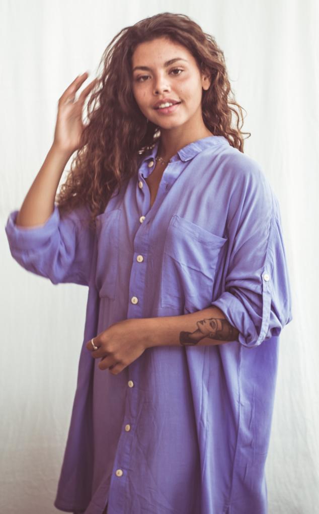 A woman wearing a sky blue, long-sleeved shirt dress with chest pockets and light coconut organic buttons.