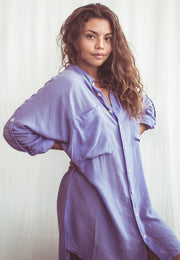 A woman wearing a sky blue, long-sleeved shirt dress with chest pockets and light coconut organic buttons.