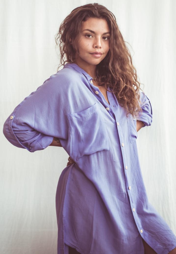 A woman wearing a sky blue, long-sleeved shirt dress with chest pockets and light coconut organic buttons.