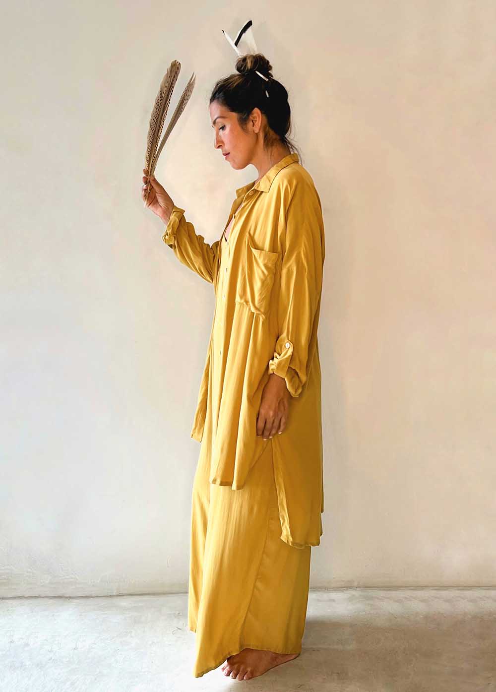Woman in a yellow outfit holding a dried plant against a plain background