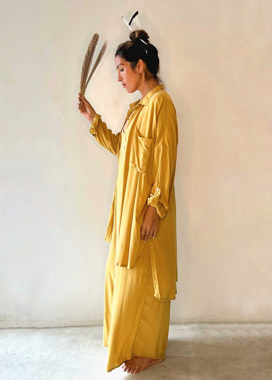 Woman in a yellow outfit holding a dried plant against a plain background
