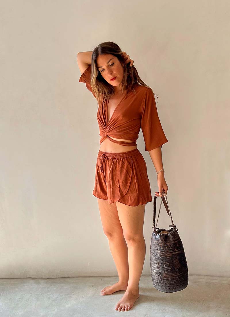 Woman in a rust-colored outfit holding a black bag against a plain background