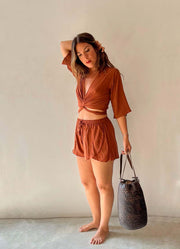 Woman in a rust-colored outfit holding a black bag against a plain background