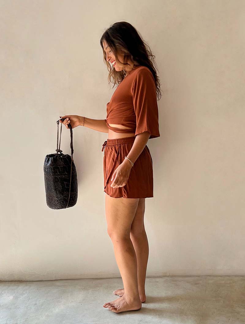 Woman in a rust-colored outfit holding a black bag against a plain background