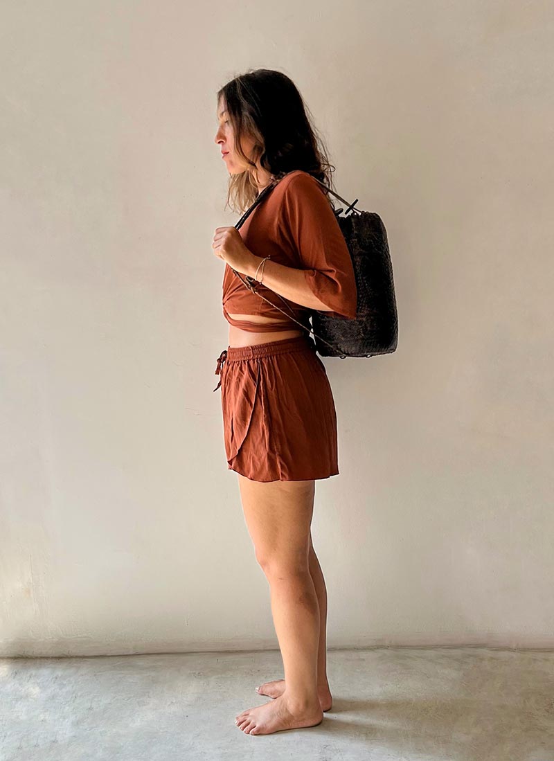 Woman in a rust-colored outfit holding a black bag against a plain background