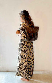 Woman in a patterned dress holding a textured bag against a plain background