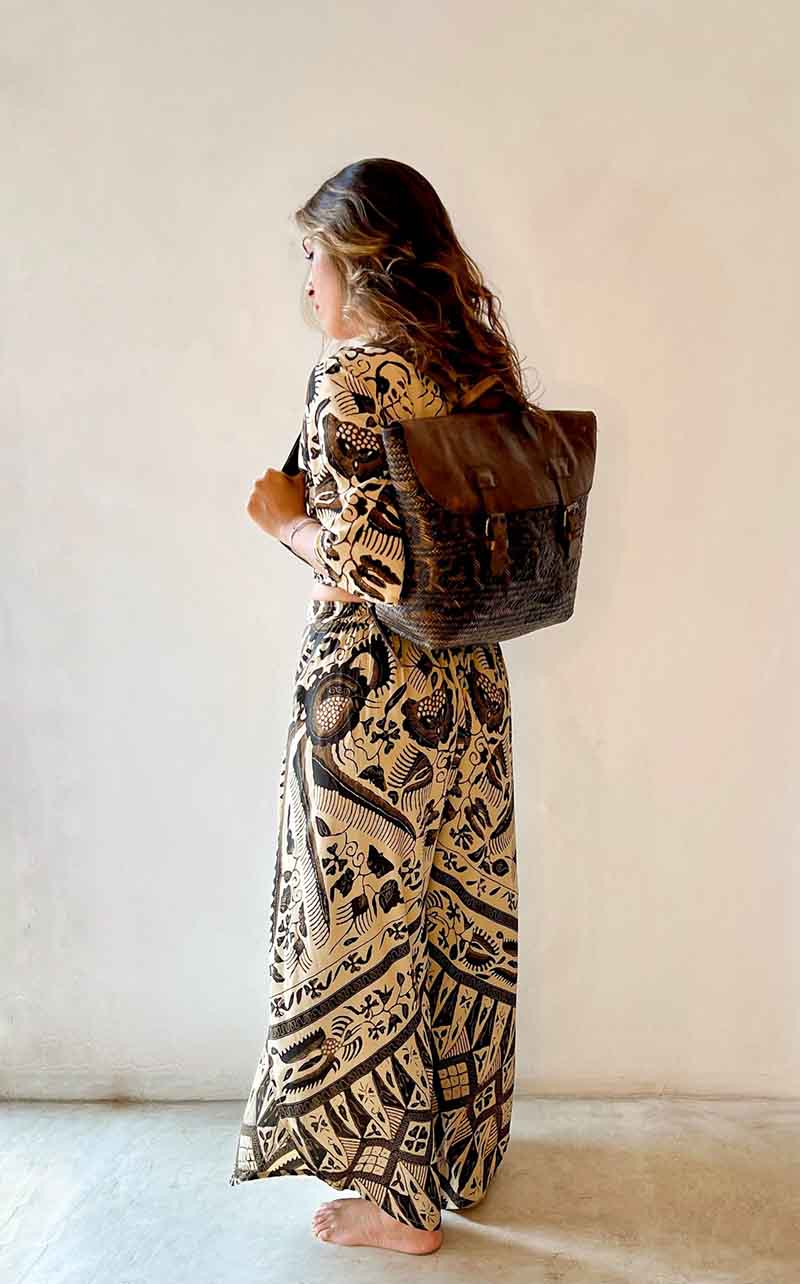 Woman in a patterned dress holding a textured bag against a plain background
