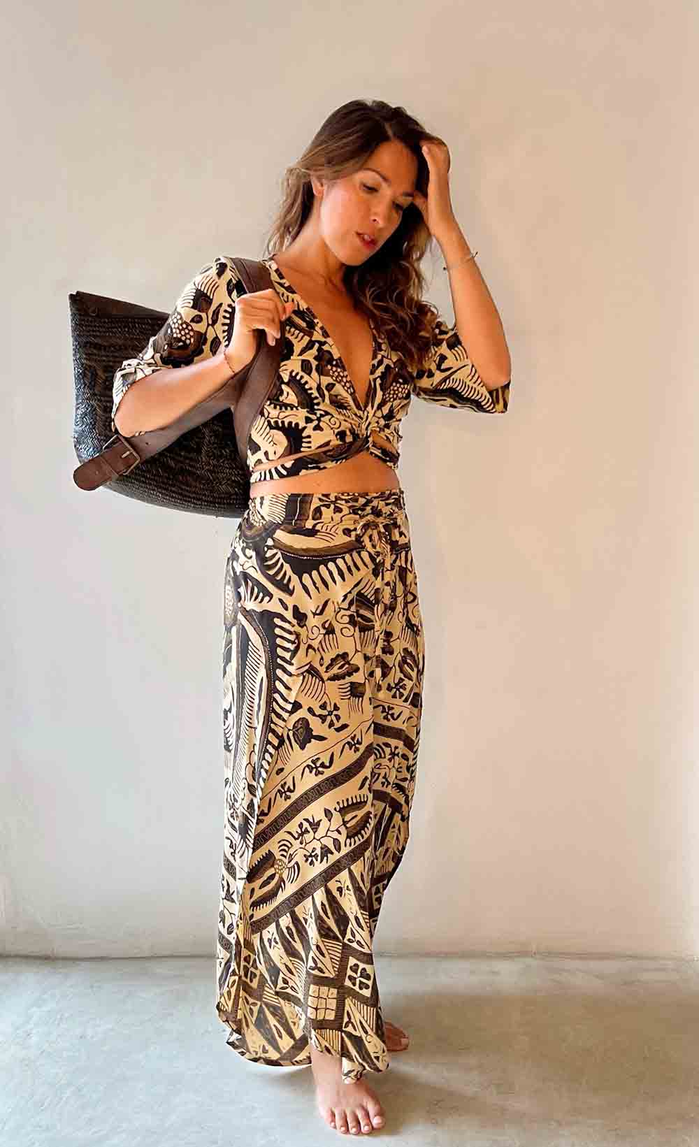 Woman wearing a patterned outfit holding a bag against a plain background
